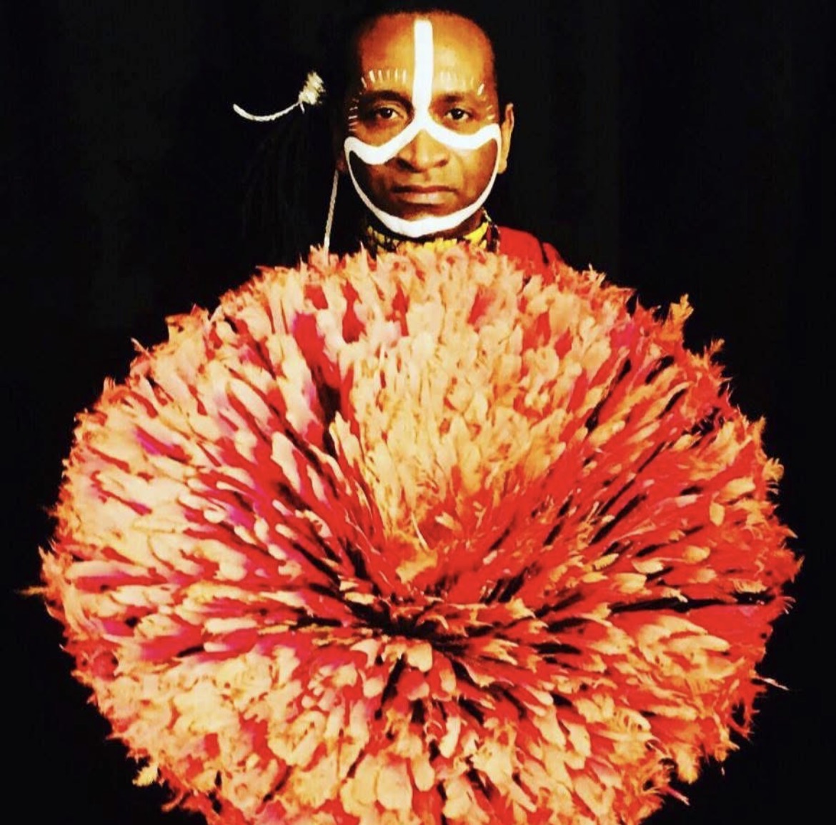 Zam Martino en costume de plumes rouges et jaunes avec maquillage blanc sur le visage