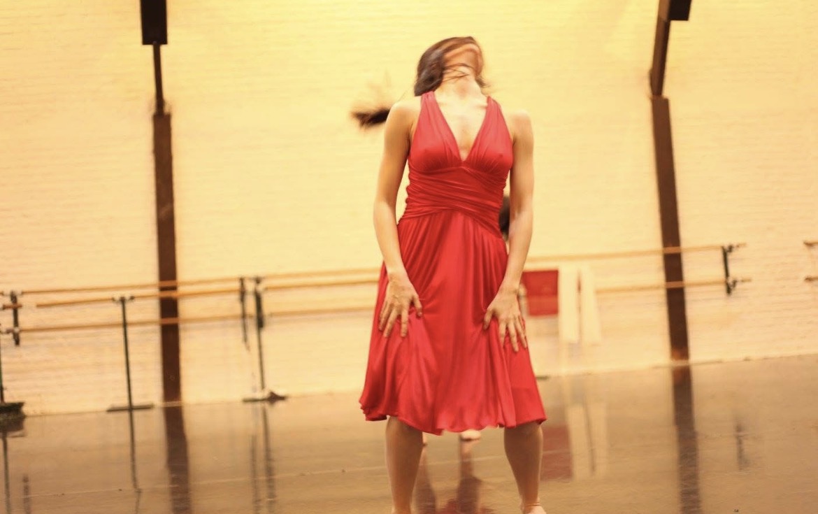 Danseuse en robe rouge, la tête rejetée en arrière, explorant l’économie du geste dans le studio