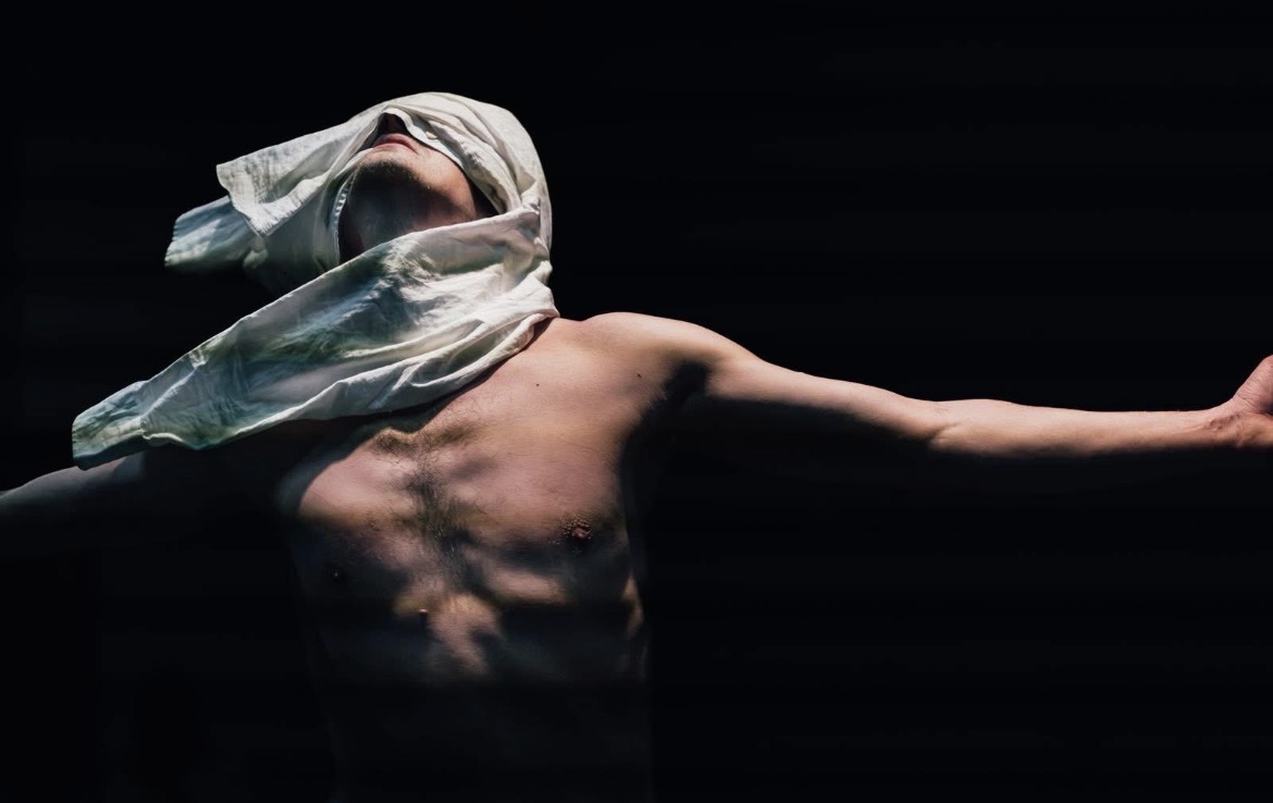 Paul Couchard, chorégraphe-interprète de La Chemise, torse nu, le visage voilé d’un tissu blanc, bras ouverts dans un élan de danse